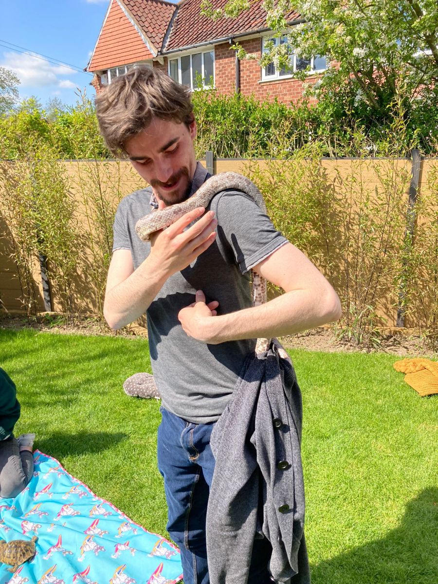a small snake wraps around a man's arm, holding his jacket in its tail